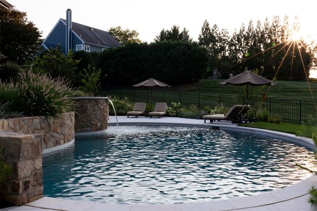 Backyard swimming pool with lounge chairs, umbrellas, and a house at sunset