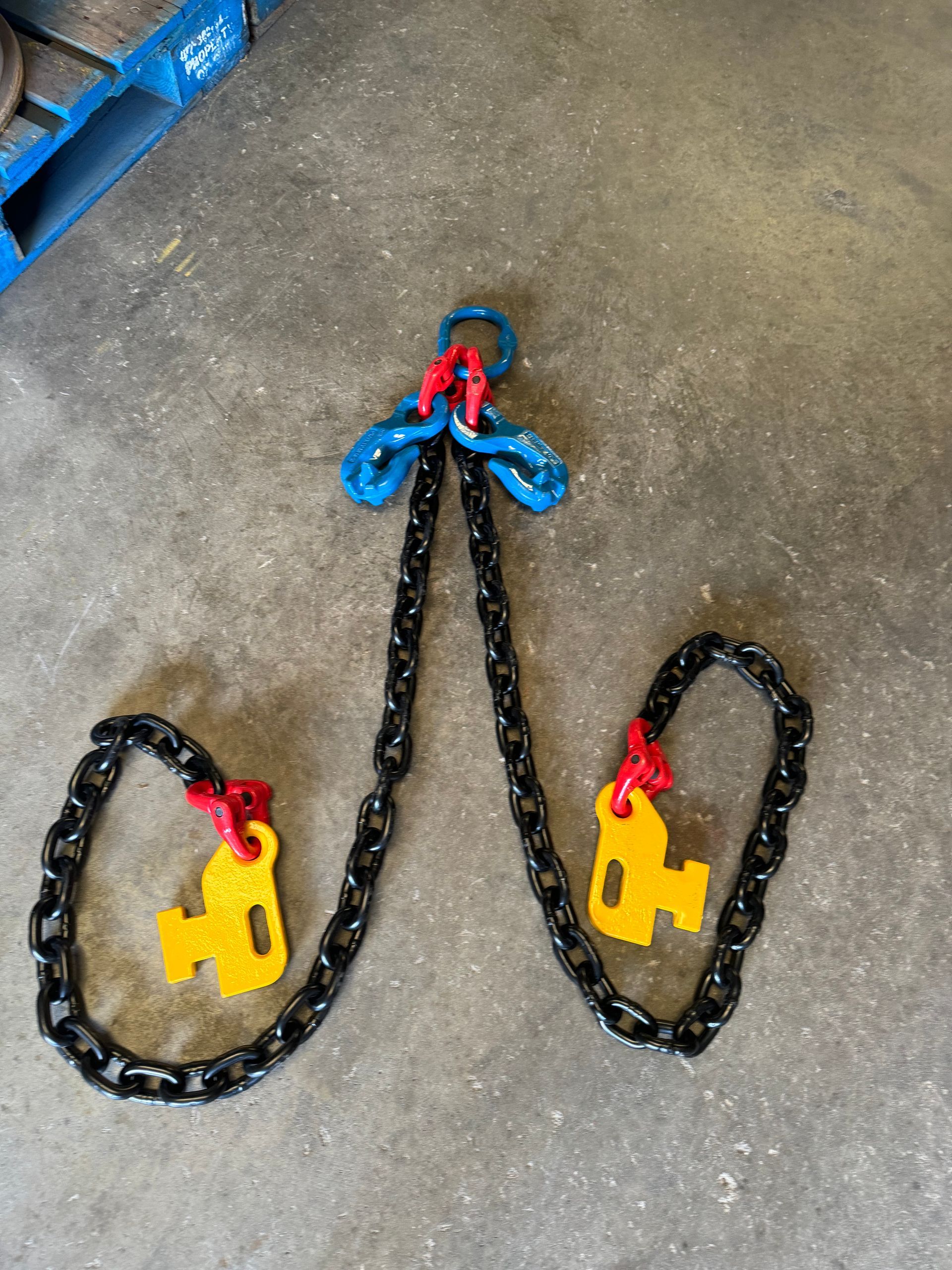 Two black chains with yellow hooks and red-blue connector links on a concrete floor