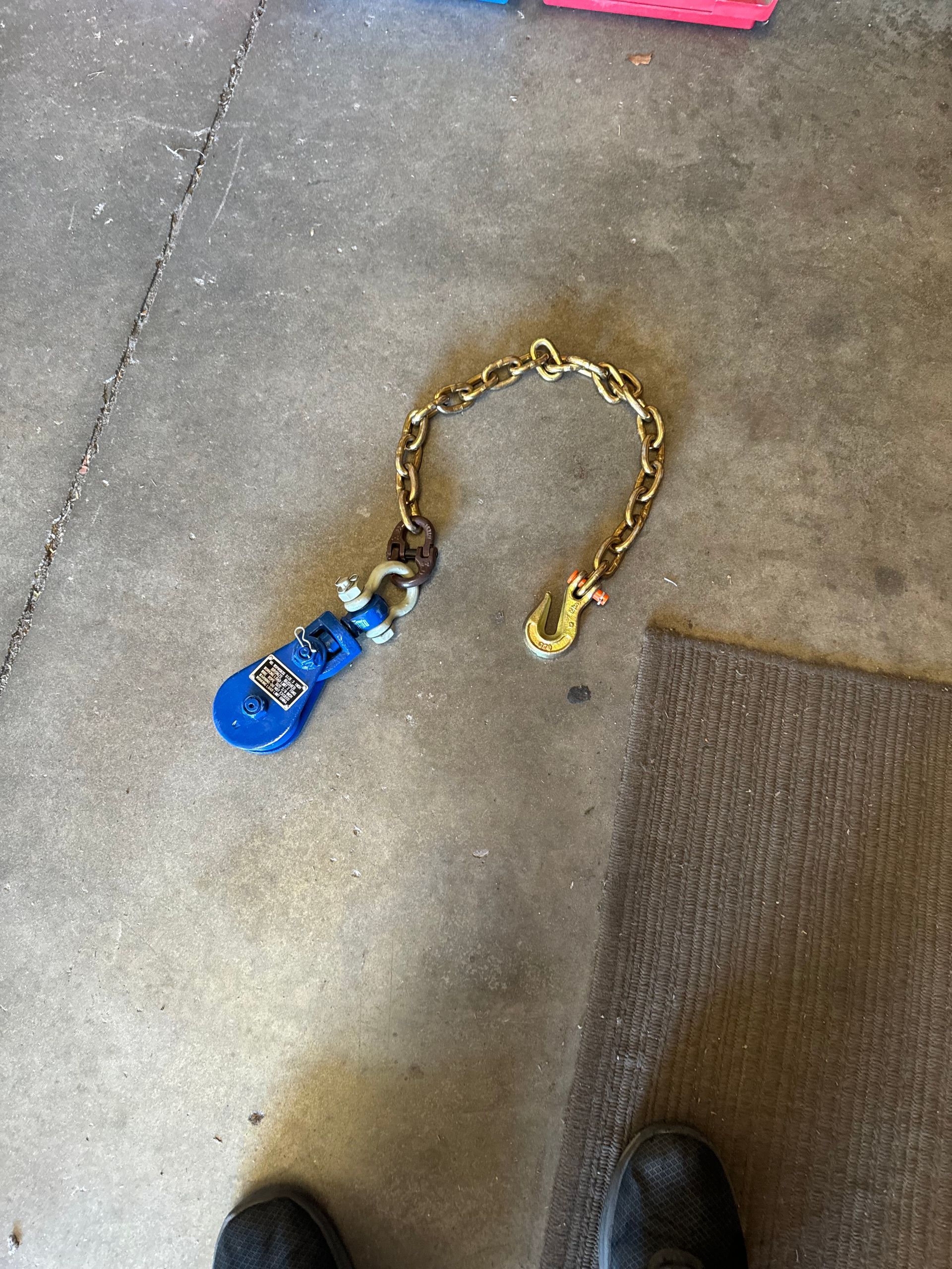 Gold chain with a blue keychain on a concrete floor near a mat and shoes.