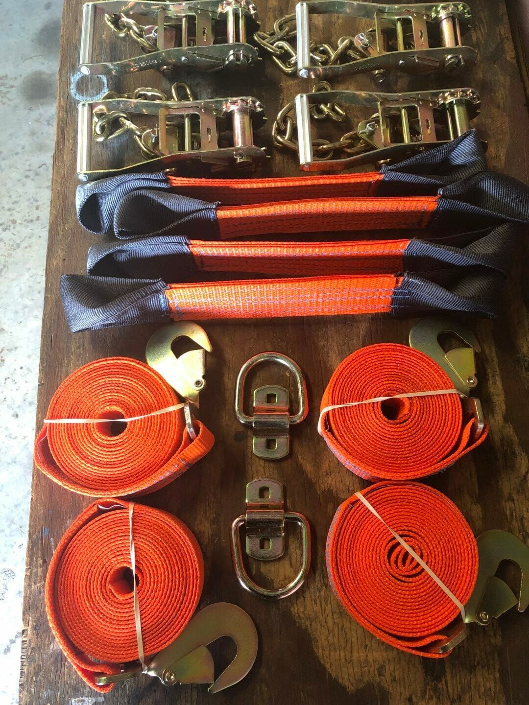 Orange tie-down straps and metal ratchet buckles neatly arranged on a floor.