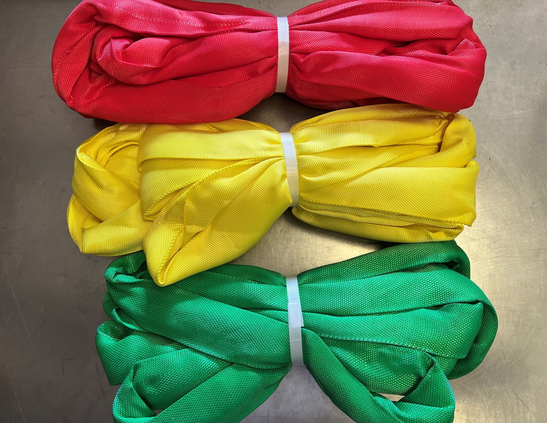 Three pairs of folded fabric bows in red, yellow, and green stacked vertically on a beige surface
