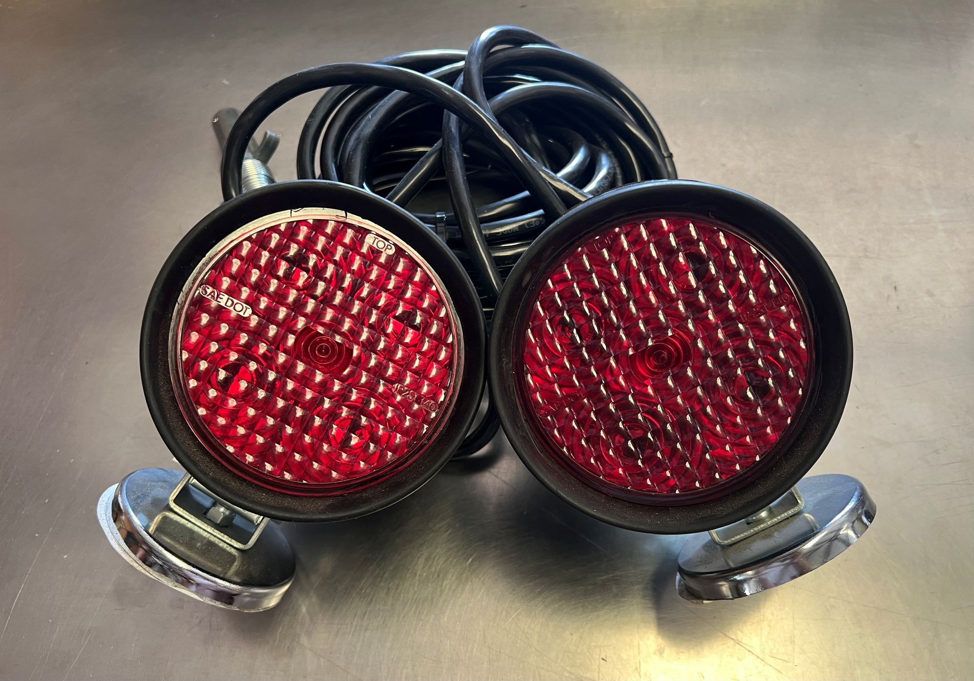 Two red round trailer lights with coiled black wiring on a metallic surface