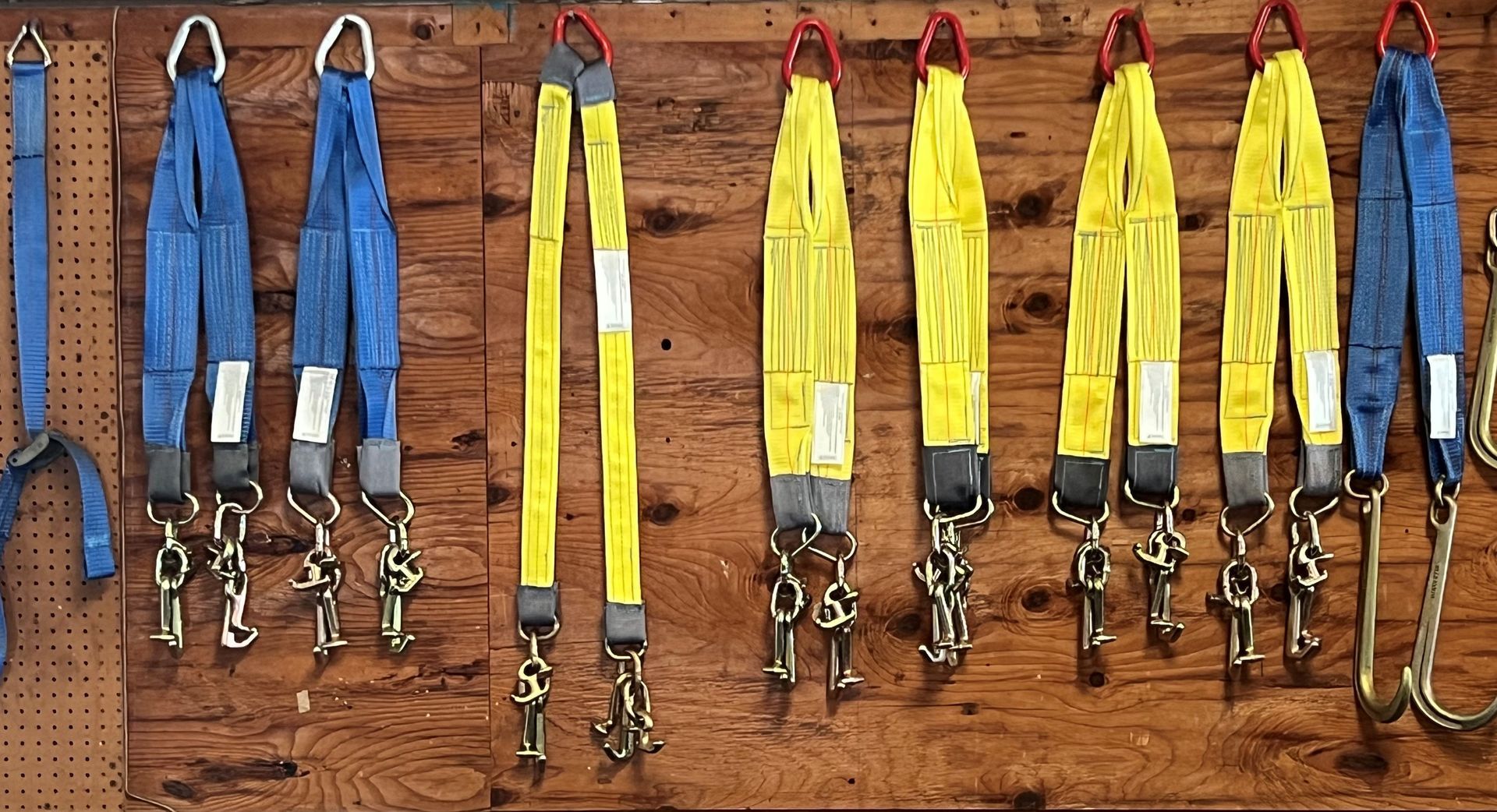 Several colorful climbing harnesses and lanyards hang in a row on a wooden wall.