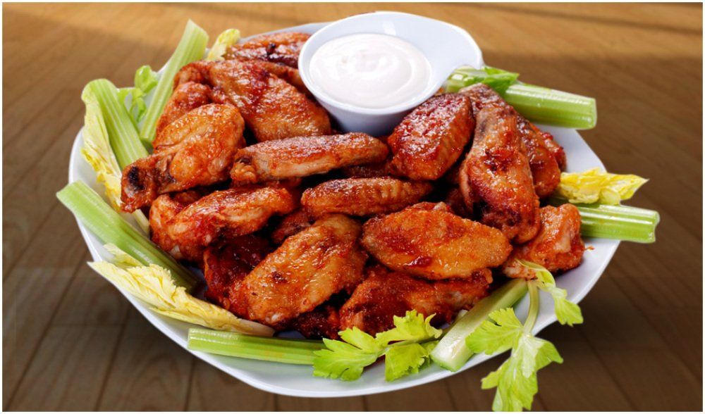 Plate of crispy chicken wings with celery sticks and a cup of ranch dip