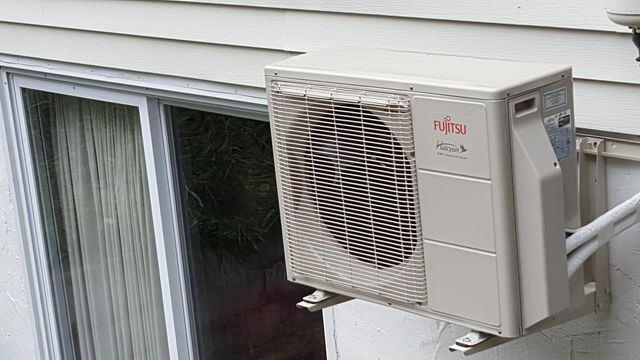 an air conditioner is mounted on the side of a building next to a window .