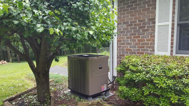 an air conditioner is sitting outside of a brick house next to a tree .