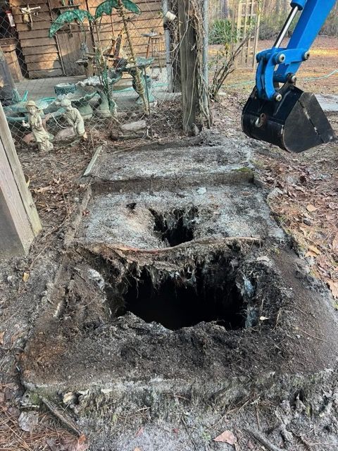 Excavator digging around a large broken concrete hole in a yard