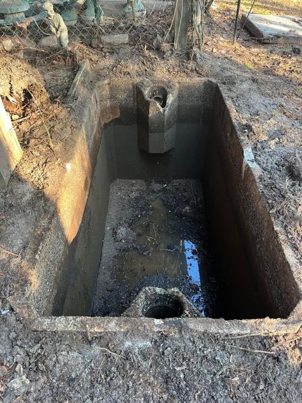Excavated rectangular pit with muddy water and a small drain hole, surrounded by dirt and concrete edges