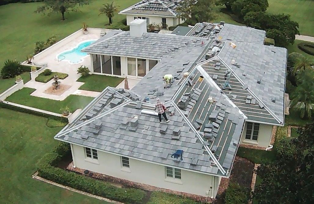 Roofers working on a house with a pool in the background. The roof is being replaced with gray tiles.
