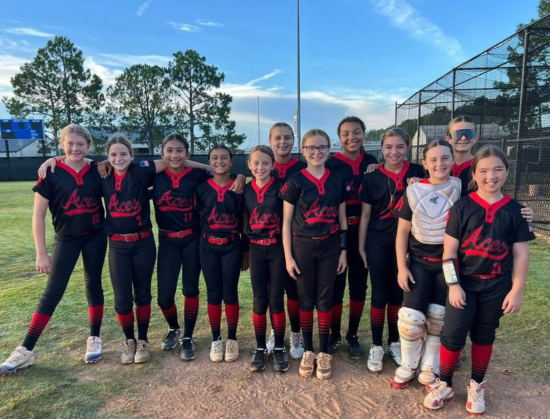 Softball team of girls in black and red uniforms, posing on a field.