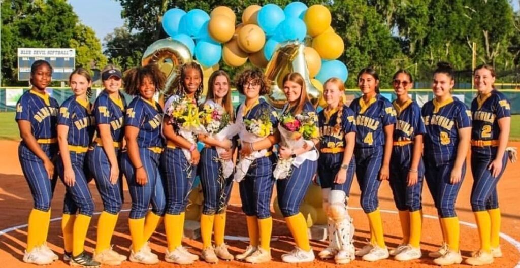 Softball team in blue and gold uniforms, posing with balloons. Celebrating 40th anniversary.