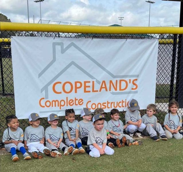 Youth baseball team in gray shirts and hats in front of a banner for Copeland's Complete Construction.