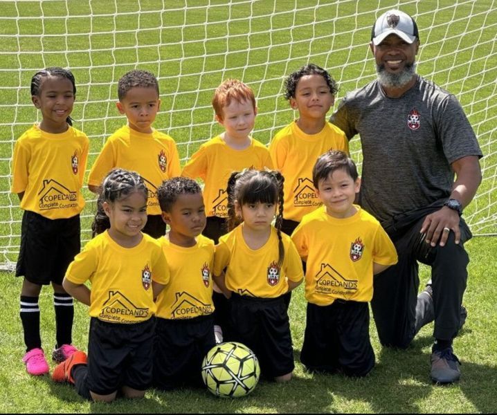 Soccer team of young children in yellow shirts with coach; green field backdrop.