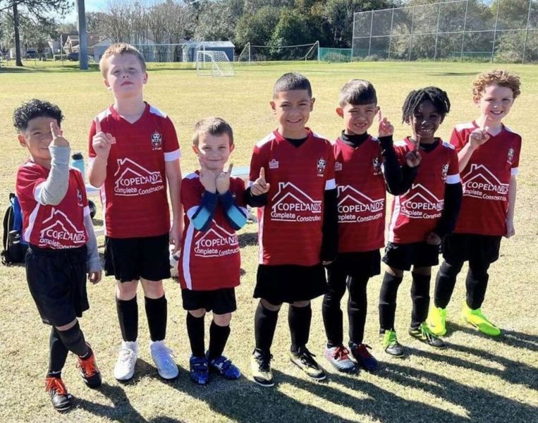 Youth soccer team in red jerseys standing on a field, some with thumbs up.