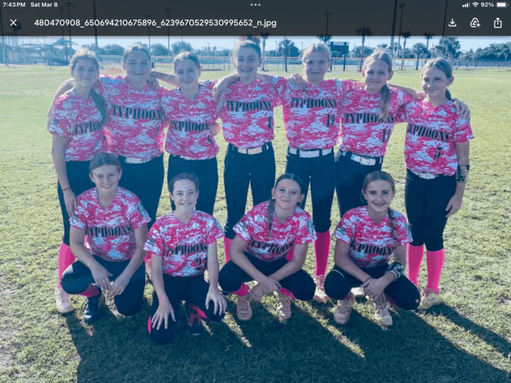 Softball team in pink camouflage jerseys poses on field.