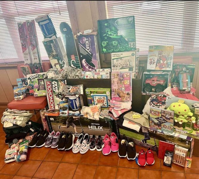 A large collection of donated gifts, including toys, shoes, and clothes, arranged in a room.