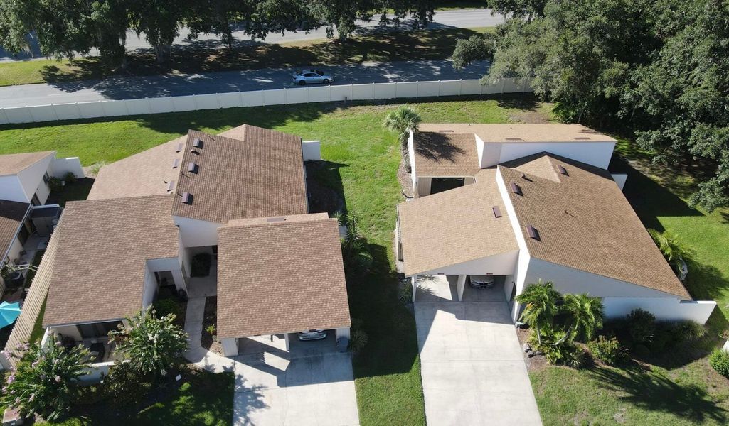 Aerial view of two houses with brown roofs, white walls, and attached carports separated by a lawn.