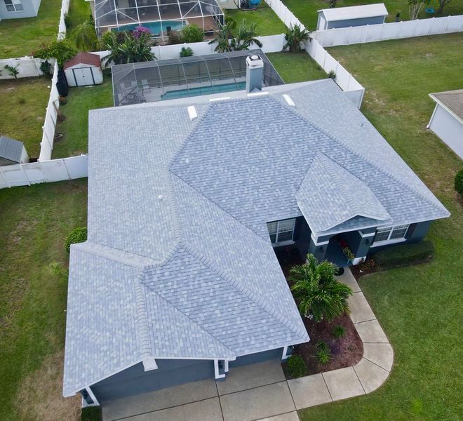 Aerial view of a house with a gray roof, a pool, and a white fence in a green yard.