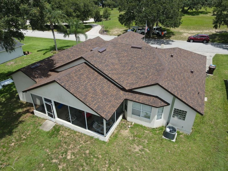 Brown roofed house with screened porch, windows, and a grassy yard.
