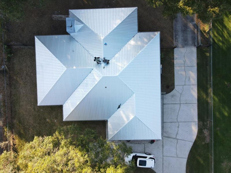Overhead view of a house with a reflective silver metal roof and a driveway next to it.