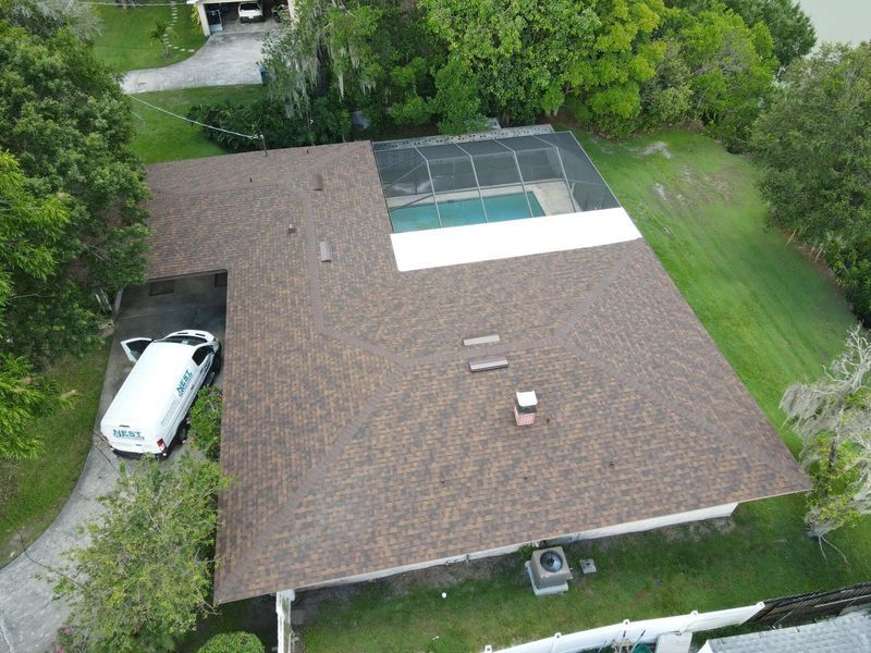 Aerial view of a house with a brown roof, pool, and a white van in the driveway.