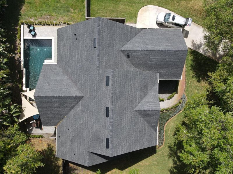 Aerial view of a house with a gray roof, a pool, and a car in the driveway.