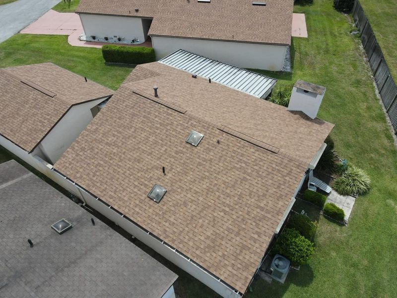 Aerial view of several houses with brown shingle roofs surrounded by green grass.