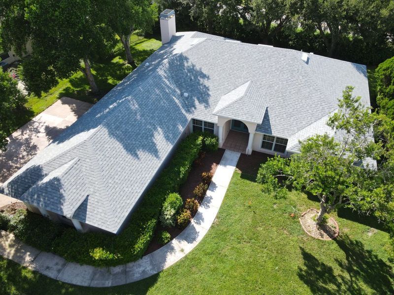 Aerial view of a white house with gray roof surrounded by green lawn and trees.