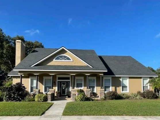 A tan one-story house with a black roof and green lawn against a clear blue sky.