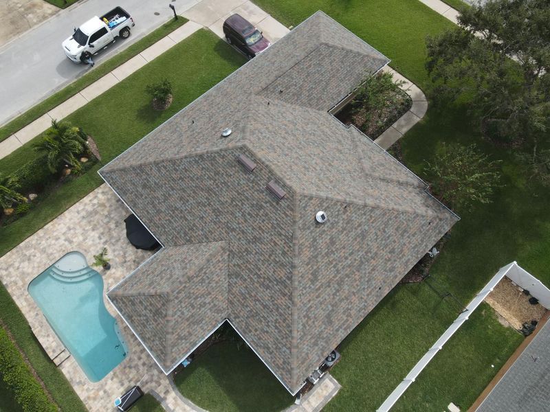 Aerial view of a house with a brown roof, pool, and green lawn in a residential area.