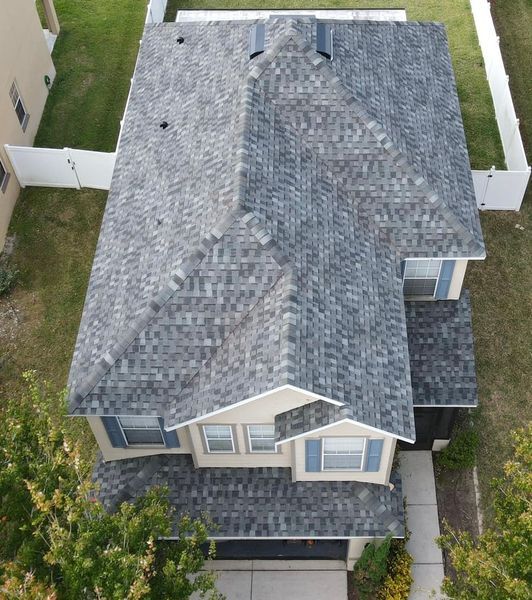 Overhead view of a two-story house with a gray shingle roof, blue shutters, and a white fence.