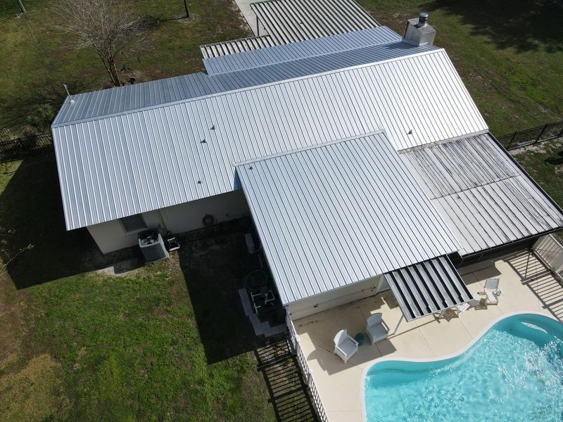 Aerial view of a house with a metal roof, pool, and patio.