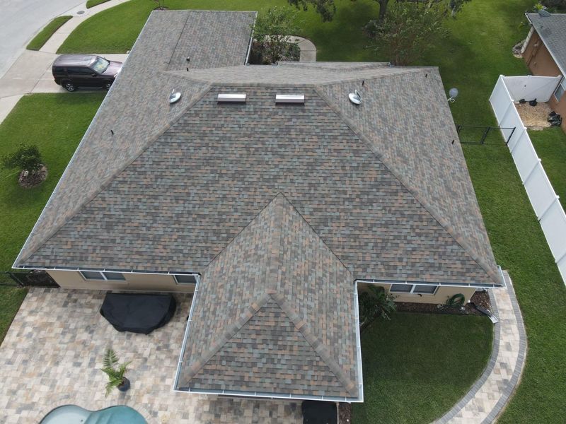 Aerial view of a house with a dark gray roof, solar tubes, a driveway, and a pool.