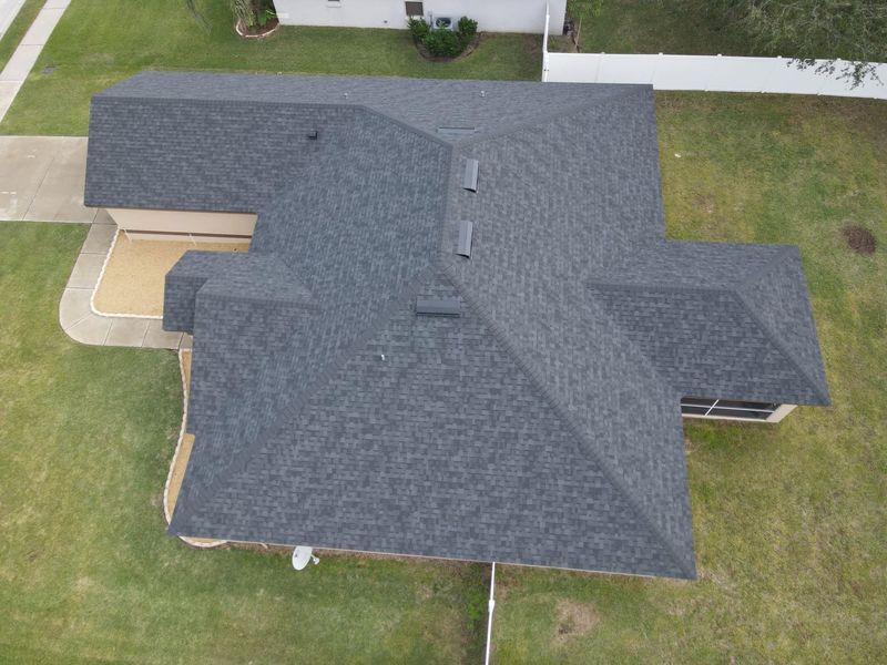 Overhead view of a gray shingle roof on a house with green lawn.