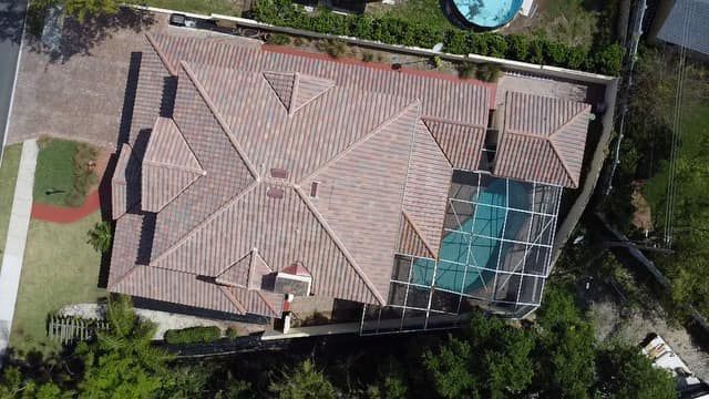 Overhead view of a house with a tile roof, pool, and yard surrounded by greenery.