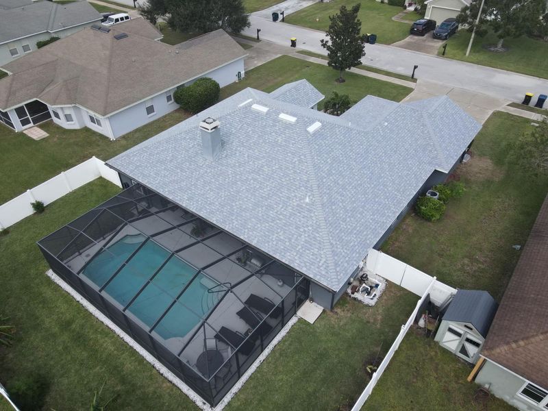 Aerial view of a house with a pool under a screened enclosure; gray roof, green lawn.