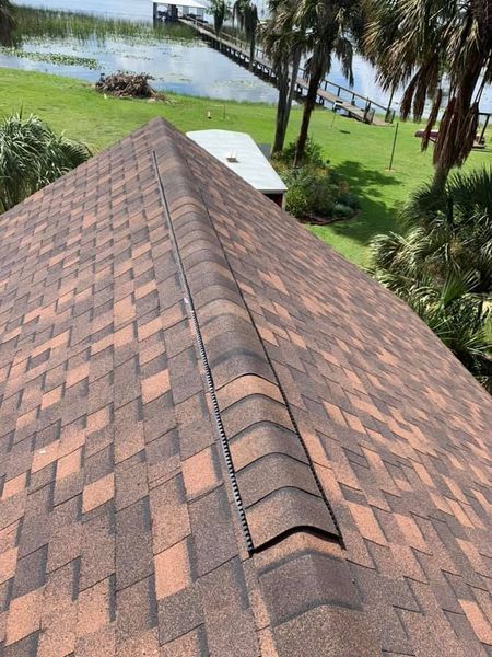 Rooftop with brown and orange shingles, ridge vent, and a lake view in the background.