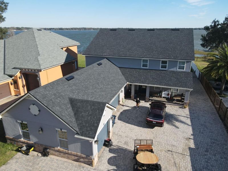 Blue house with dark gray roof, driveway with vehicles, water view.