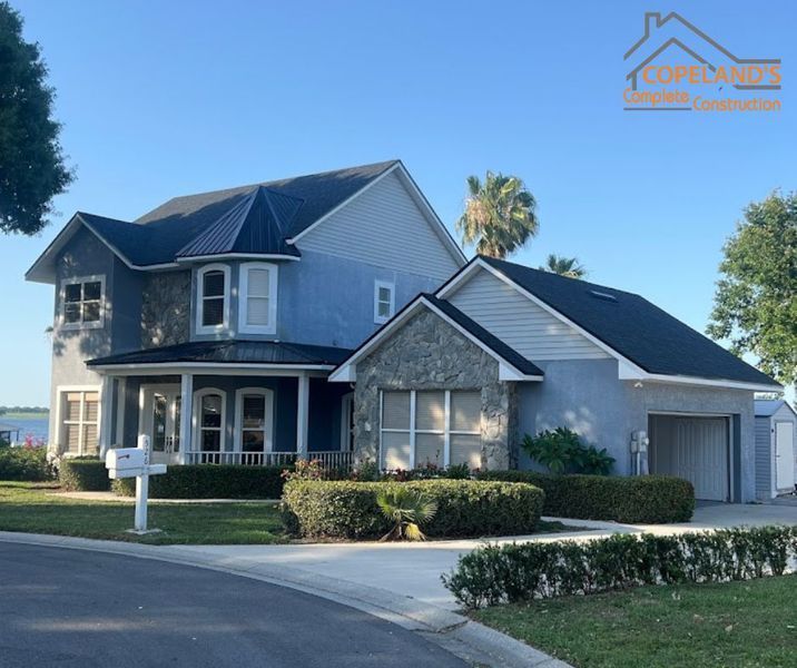 Two-story house with blue siding, stone accents, black roof, and a curved driveway.