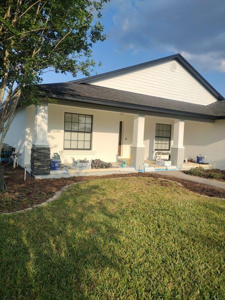 A white house with a gray roof and trim, front porch, green lawn, and a tree.