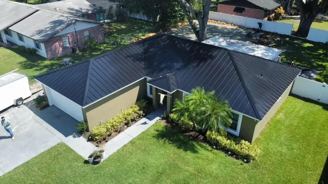 Aerial view of a house with a black metal roof, green lawn, and tan exterior.