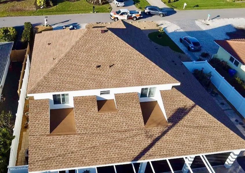 Aerial view of a house with a brown asphalt shingle roof, white walls, and a driveway.