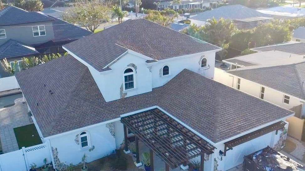 Two-story white house with brown shingle roof and pergola-covered entrance in a suburban neighborhood.