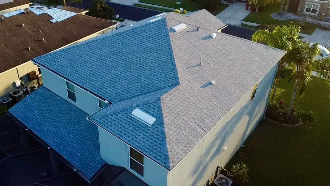 House with new gray roof, partly blue, in a suburban setting, aerial view.