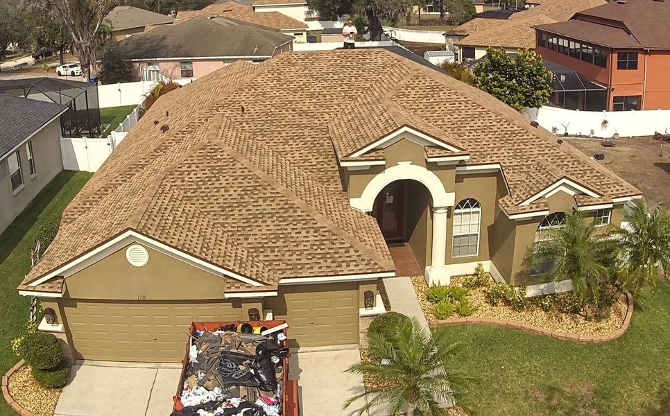Tan roof on a house with a brown exterior. A construction dumpster sits in the driveway.