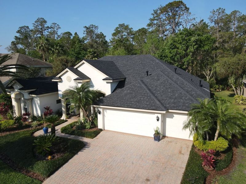 White house with a dark gray roof and attached garage, surrounded by green landscaping.