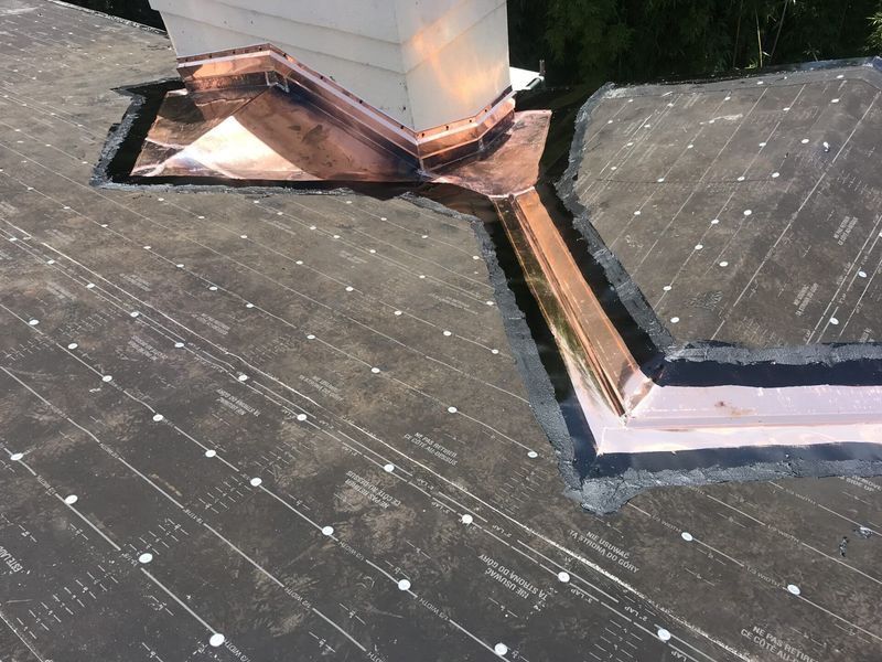 Copper flashing around a chimney on a flat roof, angled view.