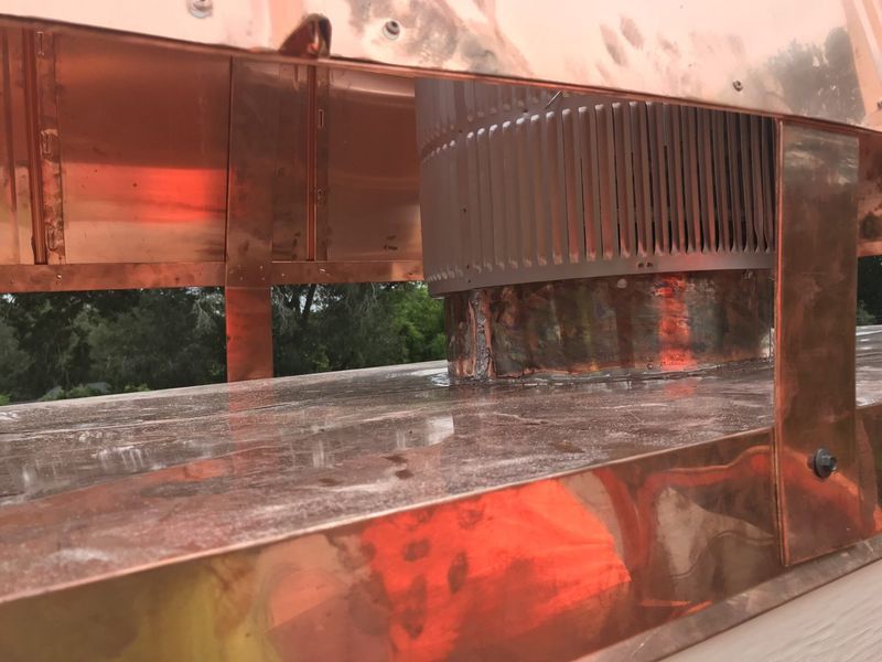 Copper chimney flashing with a metal chimney cap on a rooftop.