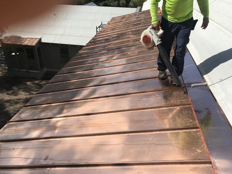 Person in green shirt using a leaf blower on a copper roof.