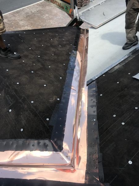 Copper flashing being installed on a dark roofing surface with a person standing nearby.